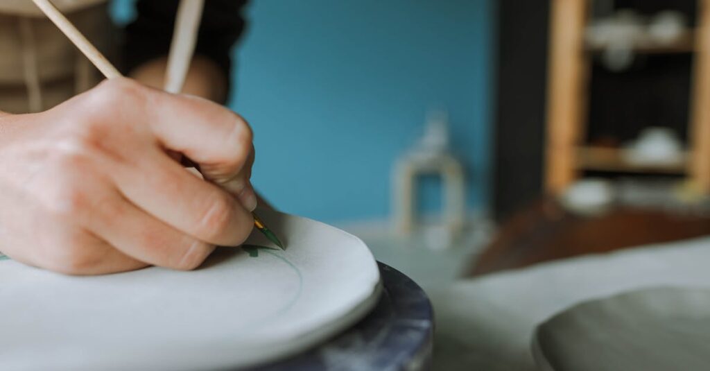 A close-up shot of a person painting pottery with a brush in a ceramics studio, displaying artistic focus.